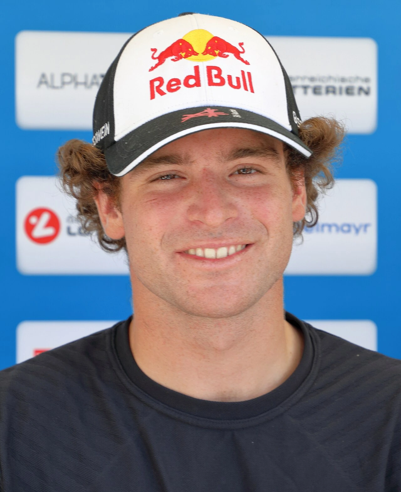 Portrait of freestyle skier Matej Svancer wearing a Red Bull cap against a sponsor backdrop