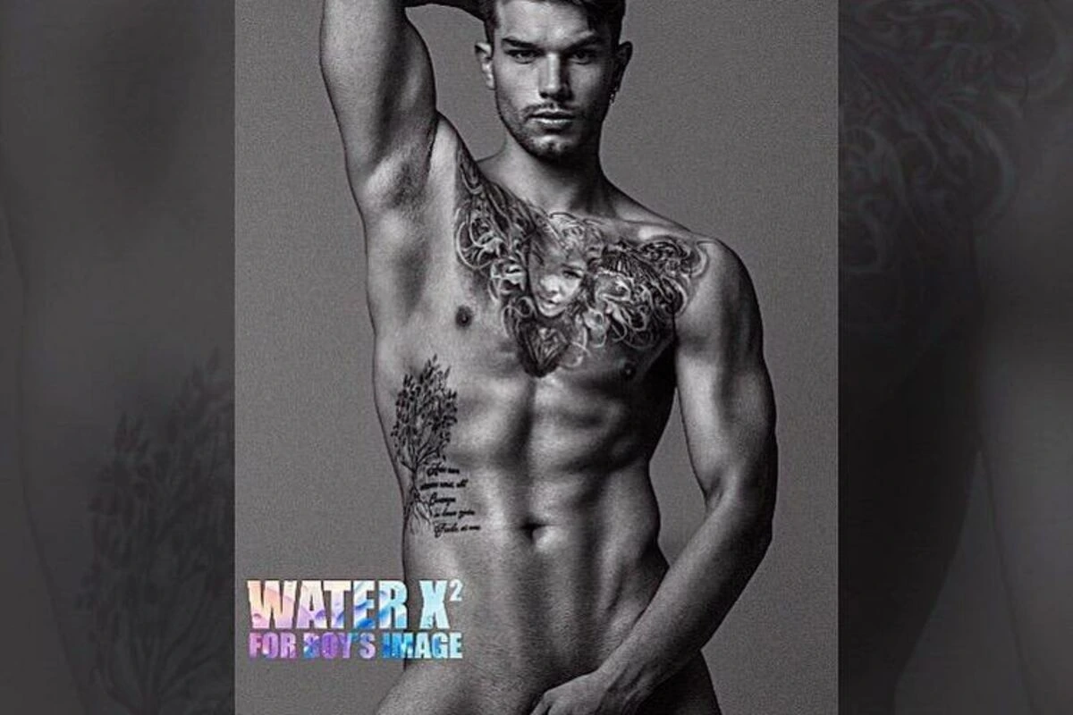 Black-and-white fashion portrait of a shirtless male model with tattoos, posed against a plain background.