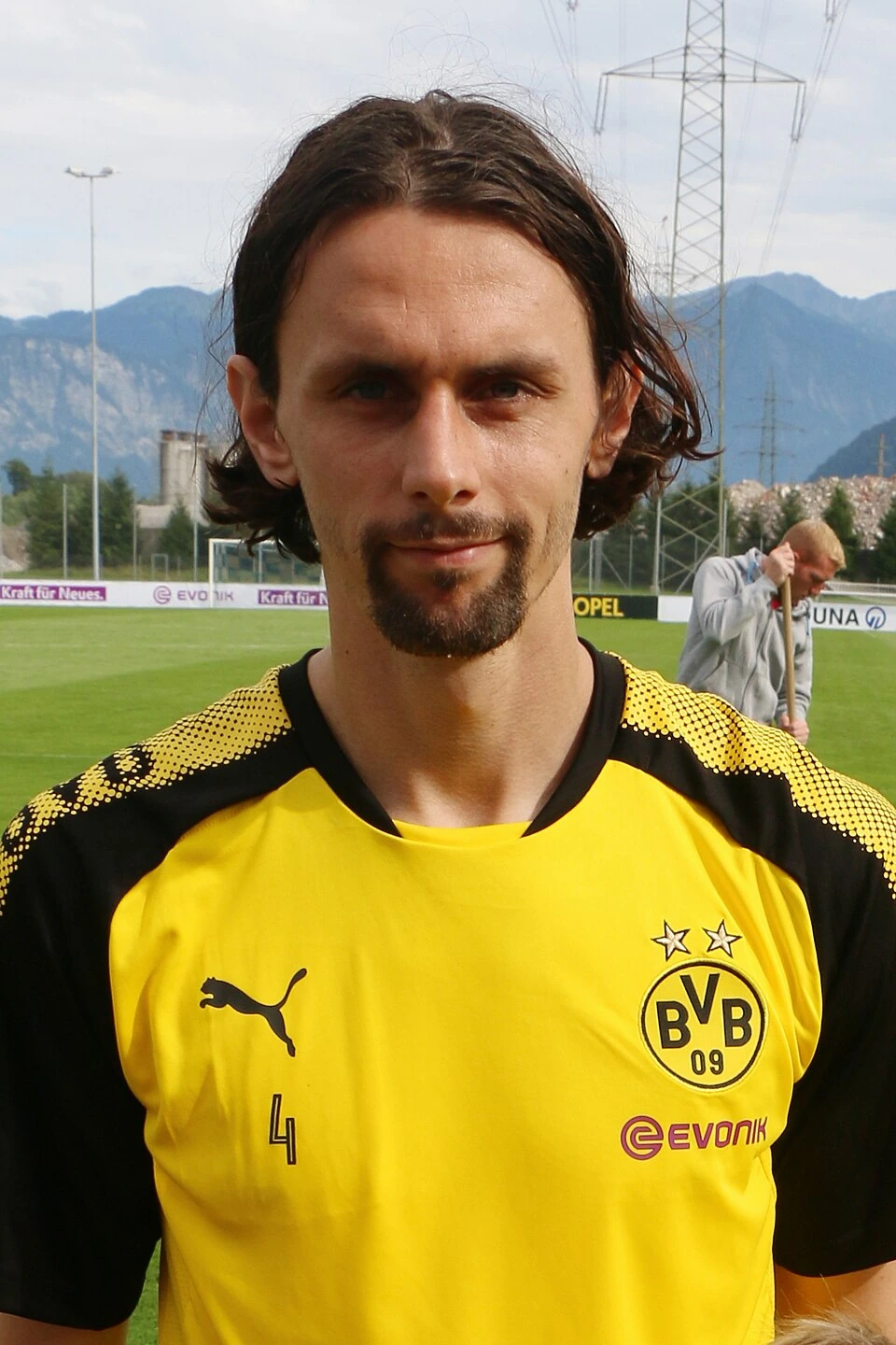 Neven Subotić in a Borussia Dortmund training jersey on a football pitch with mountains in the background